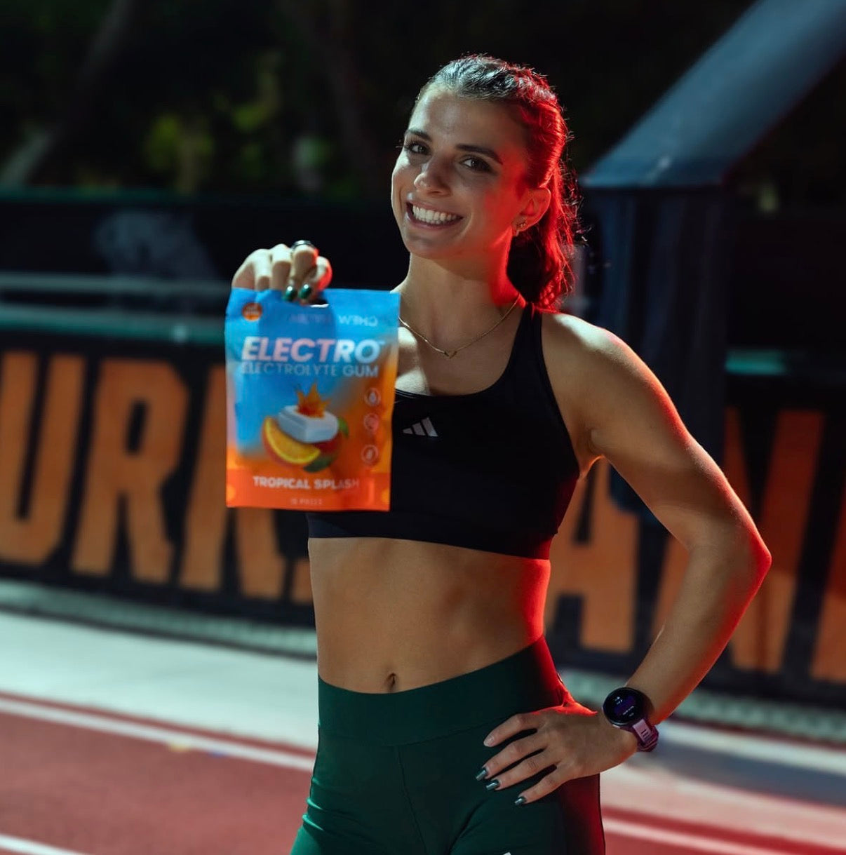 Female athlete holding Electro Tropical Splash gum pack at outdoor track