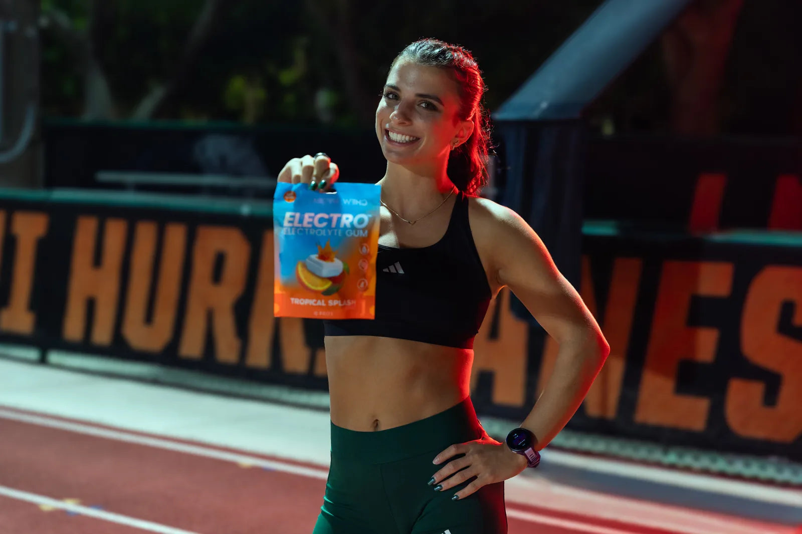 Hurricanes track athlete smiling and holding the Electro Tropical Splash pouch under stage lighting