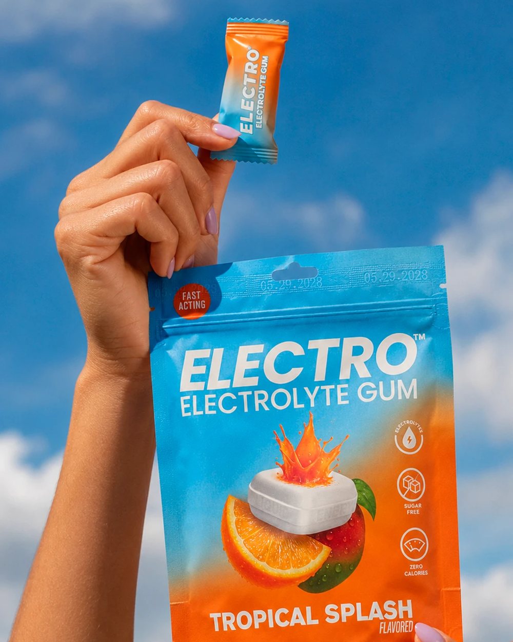 Hand holding a piece of Electro Gum and a Tropical Splash pouch against the sky