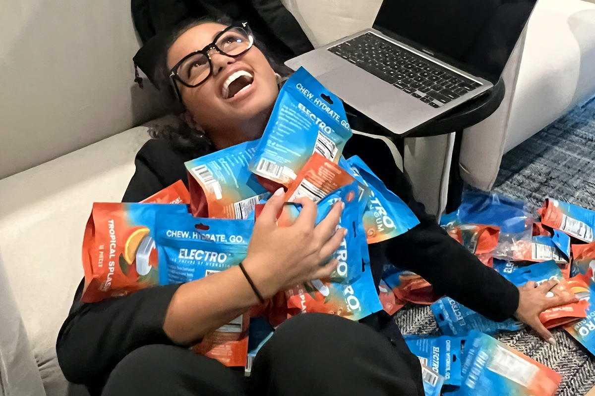Electro intern in a graduation cap laughing with an armful of Electro gum bags